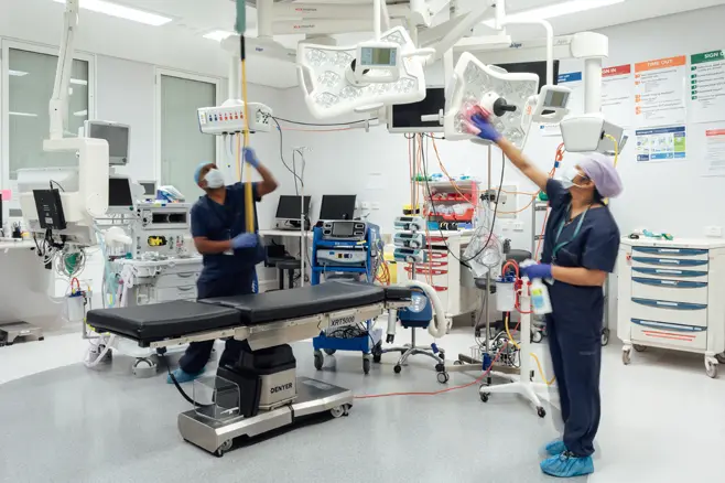 Two masked cleaners cleaning surgery room and equipment