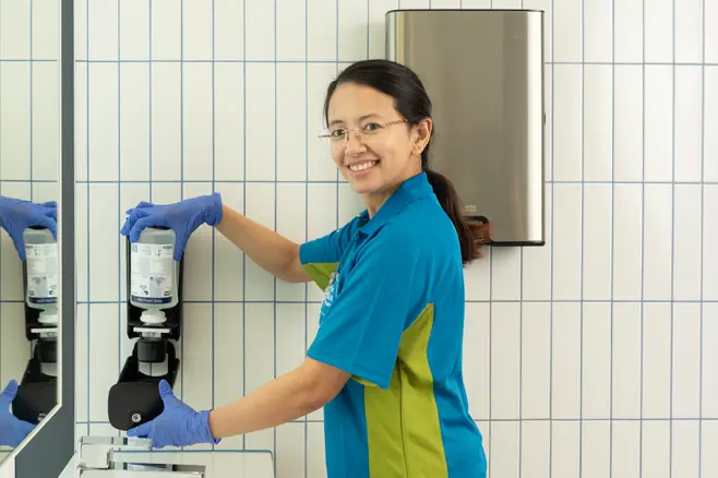 Cleaning personnel installing soap refill in office toilet dispenser