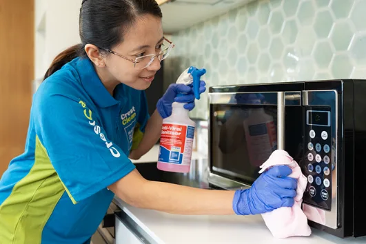 Female cleaner wiping microwave with sanitising spray